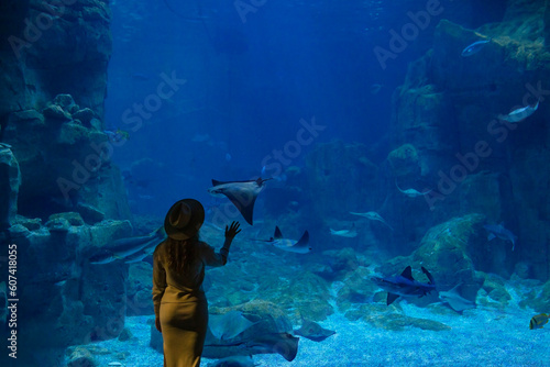 Canvas Print A young woman touches a stingray fish in an oceanarium tunnel