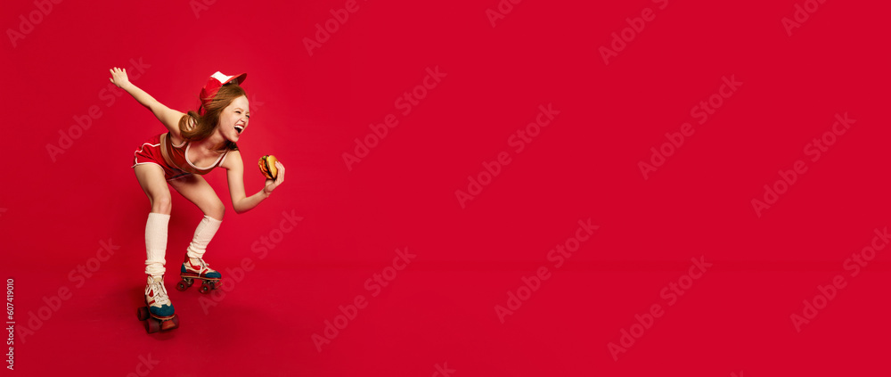 Beautiful woman, waitress on rollers with red hair holding big burger posing and smiling over red studio background. Banner with copy space Beautiful woman, waitress on rollers with red hair holding big burger posing and smiling over red studio background. Banner with copy space
