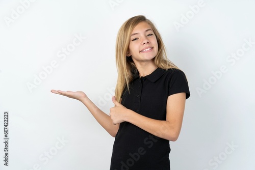 beautiful teen girl wearing black dress over white studio background Showing palm hand and doing ok gesture with thumbs up, smiling happy and cheerful. © Jihan