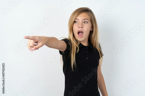 Wallpaper Mural beautiful teen girl wearing black dress over white studio background Pointing with finger surprised ahead, open mouth amazed expression, something on the front. Torontodigital.ca