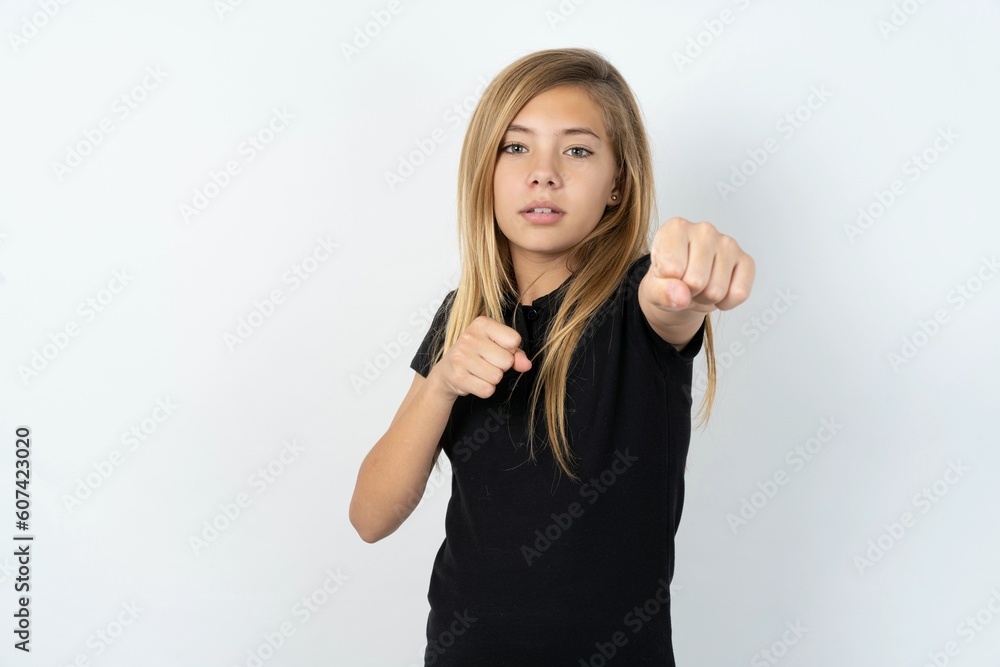 beautiful teen girl wearing black dress over white studio background Punching fist to fight, aggressive and angry attack, threat and violence