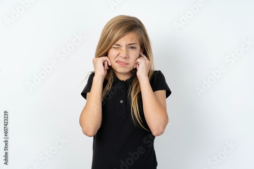 beautiful teen girl wearing black dress over white studio background covering ears with fingers with annoyed expression for the noise of loud music. Deaf concept.