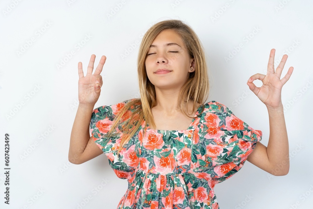beautiful teen girl wearing flowered dress over white studio background relax and smiling with eyes closed doing meditation gesture with fingers. Yoga concept. beautiful teen girl wearing flowered dress over white studio background relax and smiling with eyes closed doing meditation gesture with fingers. Yoga concept.