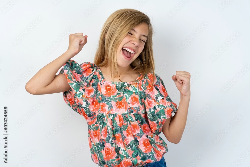 Ecstatic beautiful teen girl wearing flowered dress over white studio background shout loud yeah fist up raise win lottery Ecstatic beautiful teen girl wearing flowered dress over white studio background shout loud yeah fist up raise win lottery