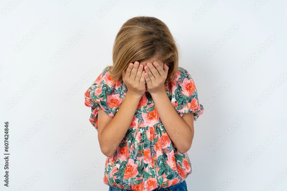 Sad beautiful teen girl wearing flowered dress over white studio background crying covering her face with her hands. Sad beautiful teen girl wearing flowered dress over white studio background crying covering her face with her hands.