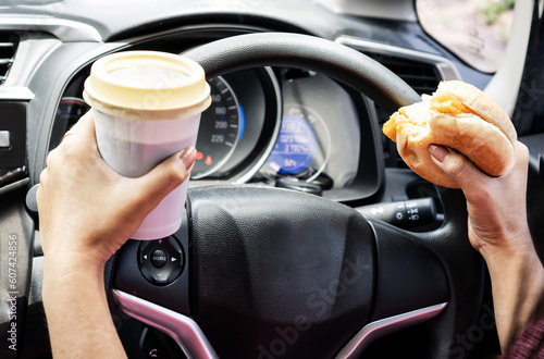 forbidden and perilous with close-up of woman's hand, holding burger and coffee, engaged in reckless eating and drinking While driving car photo