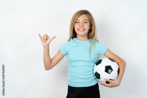 beautiful caucasian teen girl wearing sportswear holding a football ball over white wall showing up number six Liu with fingers gesture in sign Chinese language