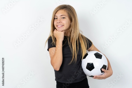Satisfied beautiful caucasian teen girl wearing sportswear  over white wall touches chin with both hands  smiles pleasantly  rejoices good day with lover