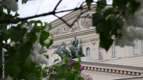 Quadriga sculpture on facade of Bolshoi Theatre building in Moscow in the background. Blurred purple lilac flowers in the foreground. Soft focus. Handheld video. Russian culture theme.