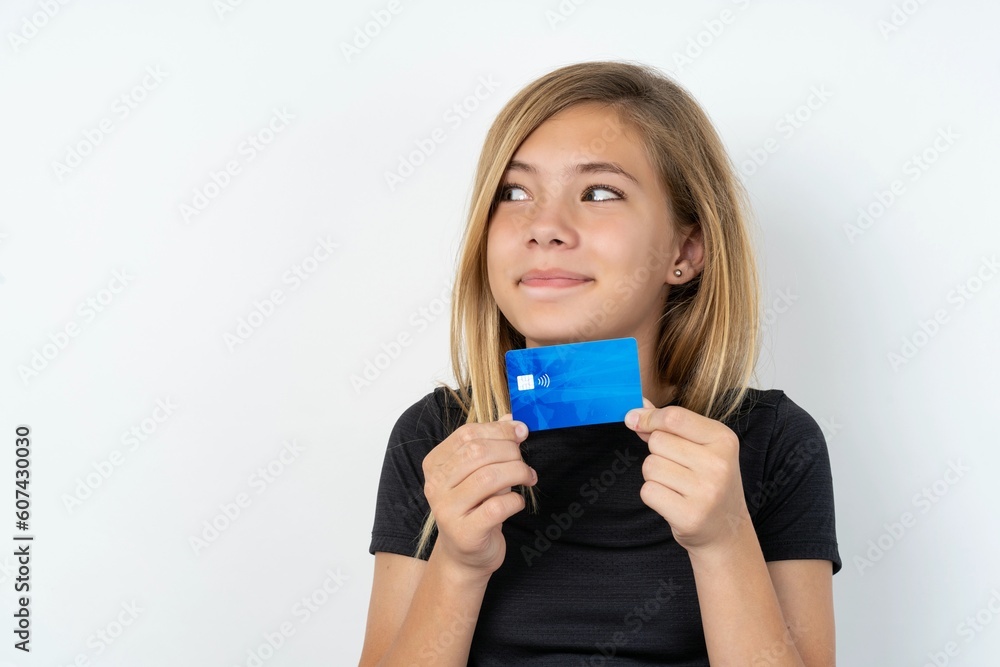 Photo of cheerful beautiful caucasian teen girl wearing sportswear over white wall hold debit card look empty space Photo of cheerful beautiful caucasian teen girl wearing sportswear over white wall hold debit card look empty space