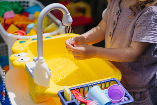 Child washes his hands and playing with toy kitchen outdoors in summer. Play area including running water. Developing Montessori toddlers activities. Kid play with water on fresh air