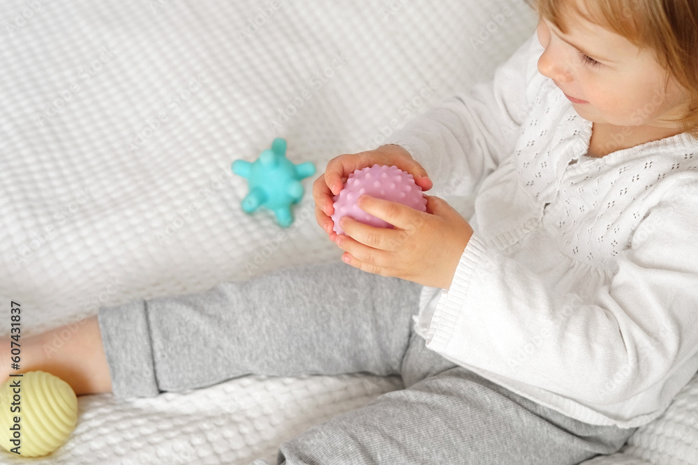 Cute baby girl playing tactile knobby balls. Young child hand plays sensory massage ball. Enhance the cognitive, physical process. Brain development. Support for Children with ADHD, autism, fidgeting Cute baby girl playing tactile knobby balls. Young child hand plays sensory massage ball. Enhance the cognitive, physical process. Brain development. Support for Children with ADHD, autism, fidgeting