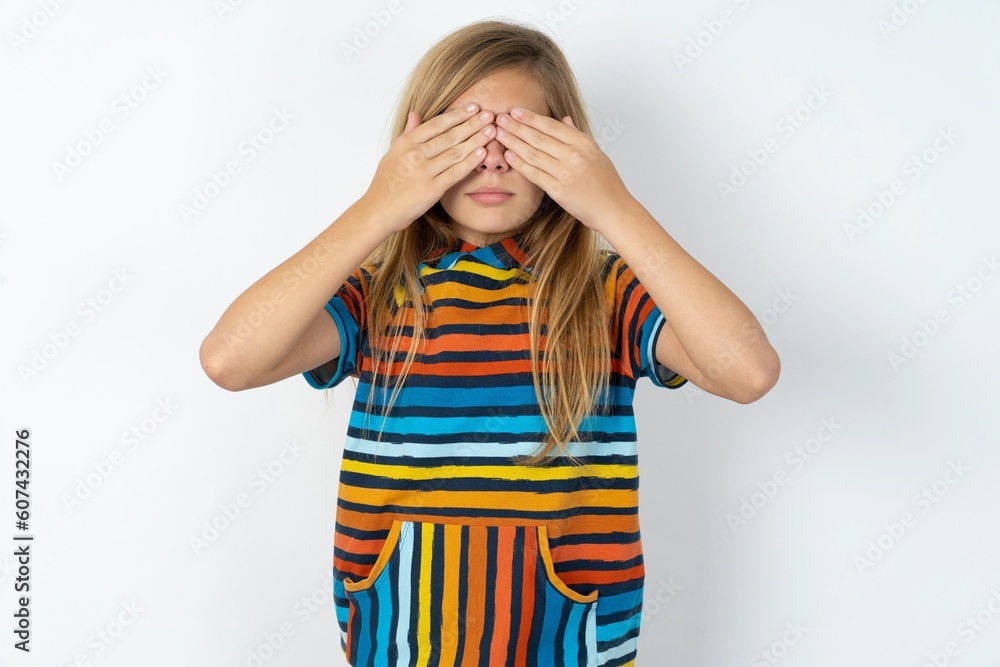 beautiful caucasian teen girl wearing striped T-shirt over white wall covering eyes with both hands, doesn't want to see anything or feeling ashamed. Human feelings reactions. beautiful caucasian teen girl wearing striped T-shirt over white wall covering eyes with both hands, doesn't want to see anything or feeling ashamed. Human feelings reactions.