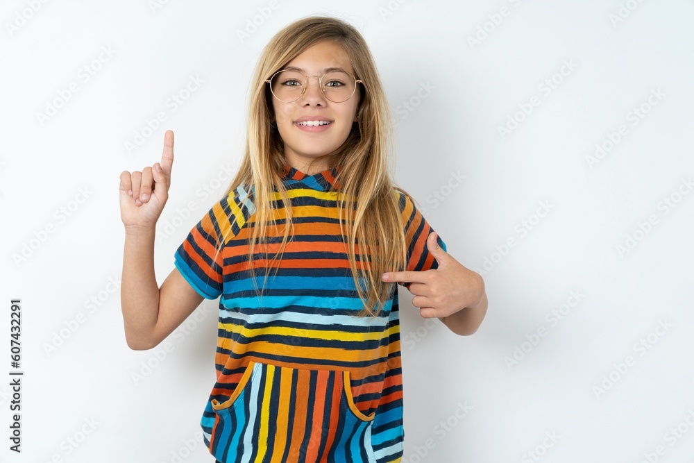 beautiful caucasian teen girl wearing striped T-shirt over white wall says: wow how exciting it is, has amazed expression, indicates something. One hand on her chest and pointing with other hand. beautiful caucasian teen girl wearing striped T-shirt over white wall says: wow how exciting it is, has amazed expression, indicates something. One hand on her chest and pointing with other hand.