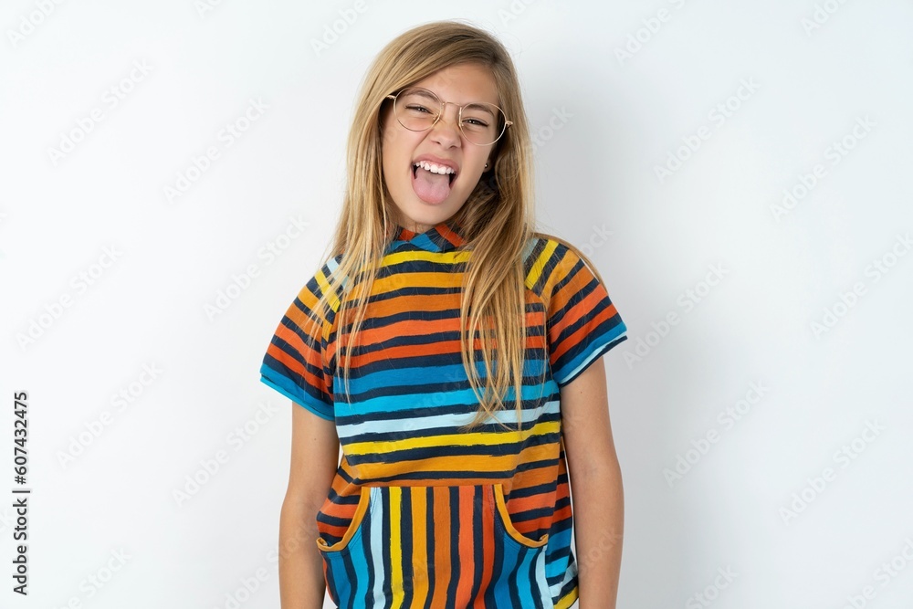 beautiful caucasian teen girl wearing striped T-shirt over white wall with happy and funny face smiling and showing tongue. beautiful caucasian teen girl wearing striped T-shirt over white wall with happy and funny face smiling and showing tongue.