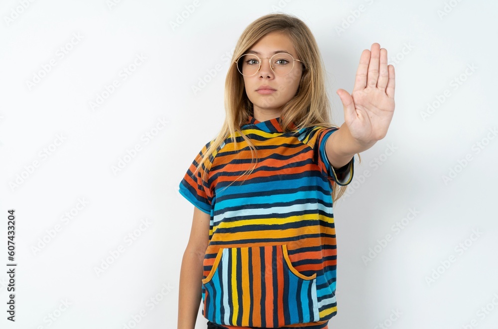 beautiful caucasian teen girl wearing striped T-shirt over white wall doing stop gesture with palm of the hand. Warning expression with negative and serious gesture on the face. beautiful caucasian teen girl wearing striped T-shirt over white wall doing stop gesture with palm of the hand. Warning expression with negative and serious gesture on the face.