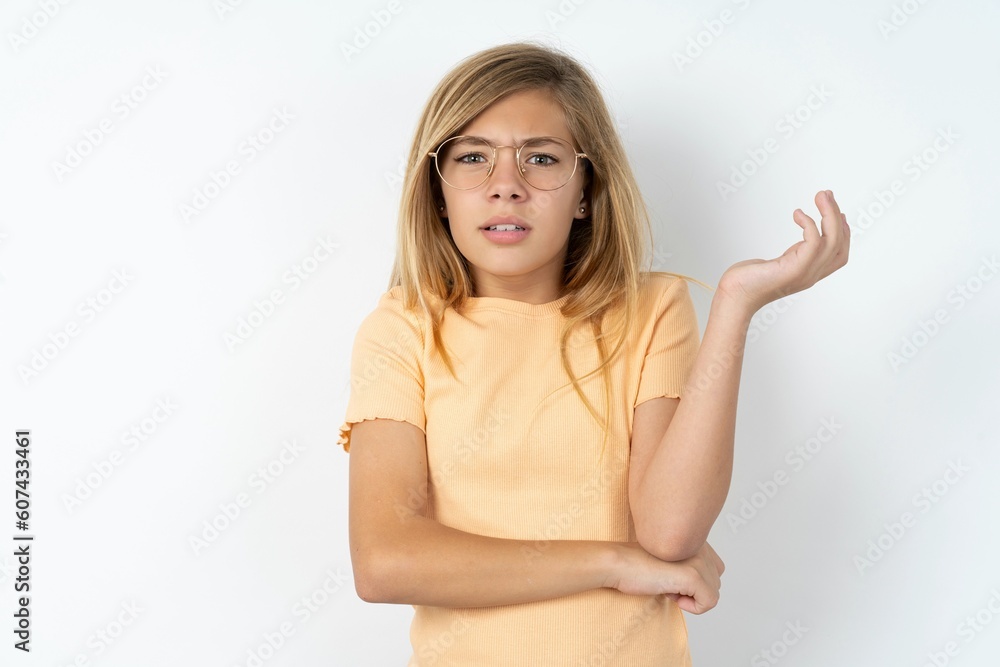 Studio shot of frustrated beautiful caucasian teen girl wearing orange T-shirt over white wall gesturing with raised palm, frowning, being displeased and confused with dumb question. Studio shot of frustrated beautiful caucasian teen girl wearing orange T-shirt over white wall gesturing with raised palm, frowning, being displeased and confused with dumb question.