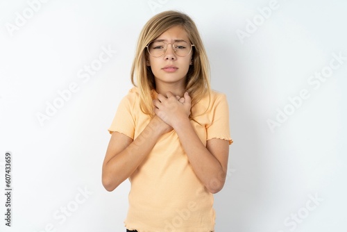 Sad beautiful caucasian teen girl wearing orange T-shirt over white wall feeling upset while spending time at home alone staring at camera with unhappy or regretful look.