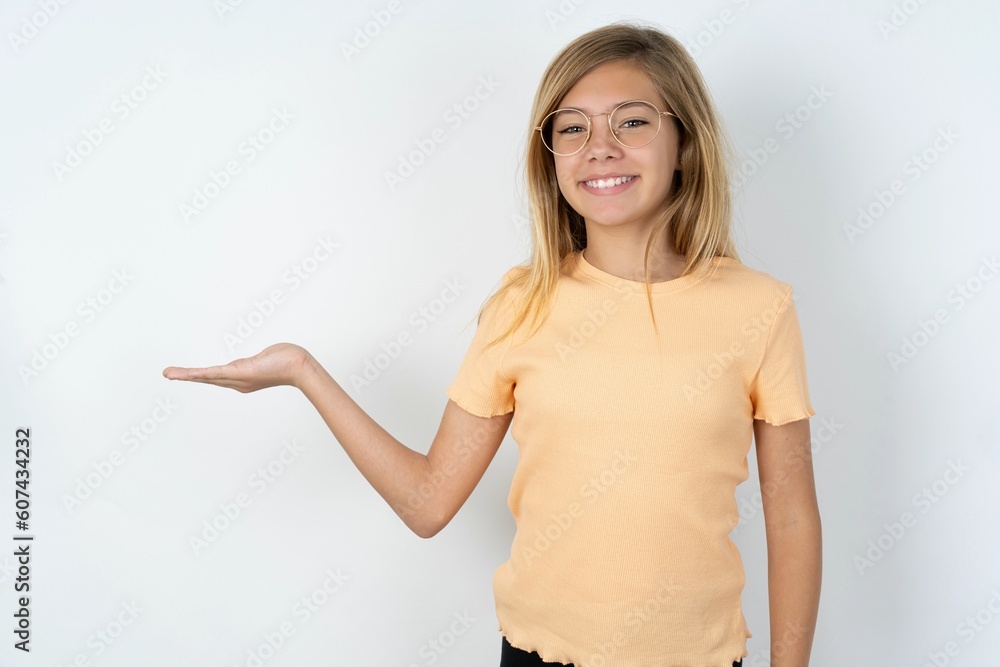 Positive glad beautiful caucasian teen girl wearing orange T-shirt over white says: wow how exciting it is, has amazed expression, shows something on blank space with open hand. Advertisement concept.