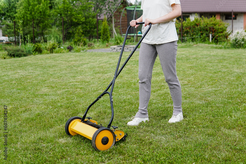 Young woman mowing lawn with a manual push lawn mower - obrazy, fototapety, plakaty 