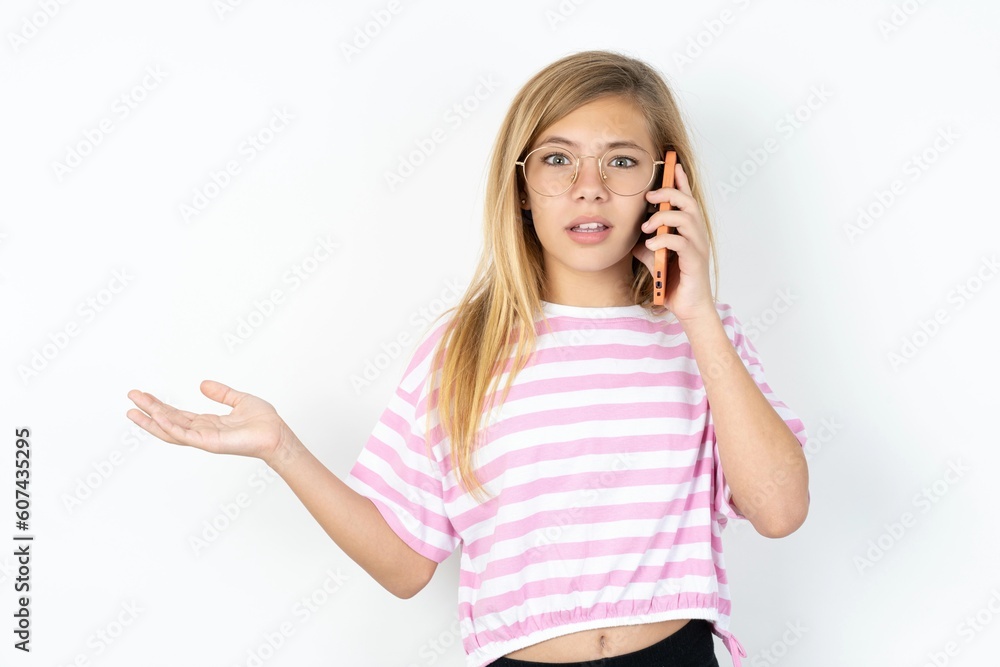 Happy beautiful caucasian teen girl wearing striped T-shirt over white wall sending a message on his smartphone or taking a selfie and making ok sign with his hand. Happy beautiful caucasian teen girl wearing striped T-shirt over white wall sending a message on his smartphone or taking a selfie and making ok sign with his hand.