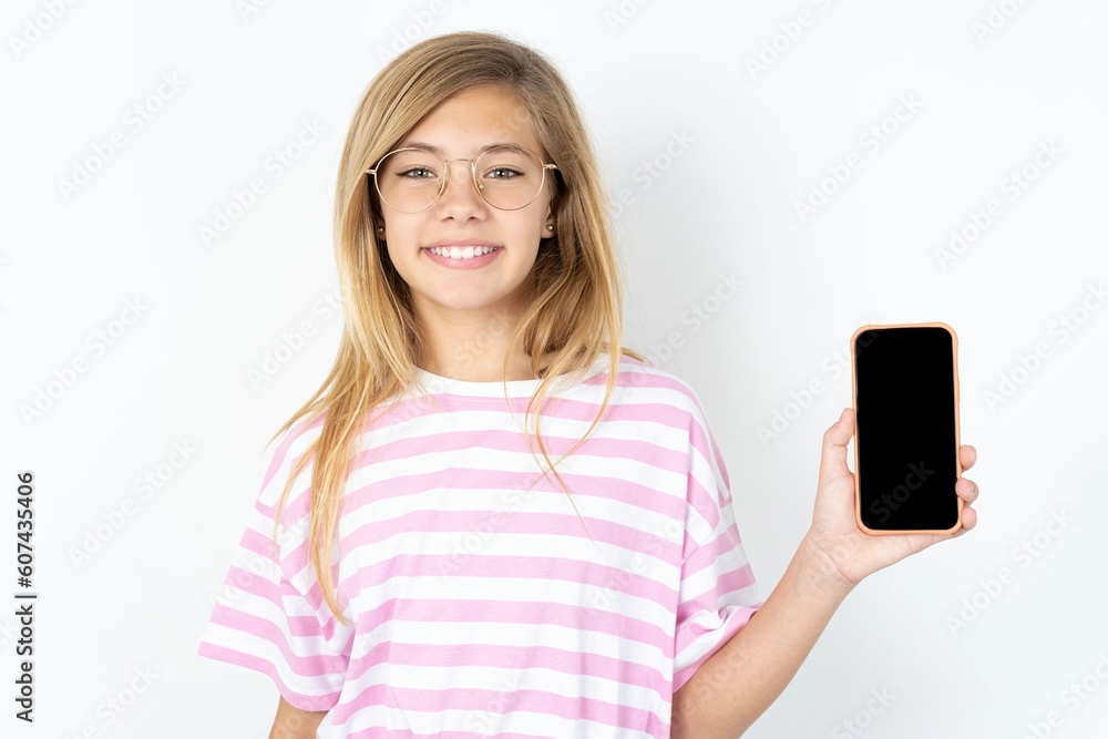 Portrait of happy friendly beautiful caucasian teen girl wearing striped T-shirt over white wall taking selfie and waving hand, communicating on video call, online chatting. Portrait of happy friendly beautiful caucasian teen girl wearing striped T-shirt over white wall taking selfie and waving hand, communicating on video call, online chatting.