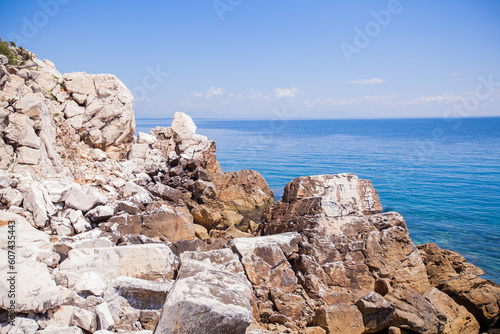  Hidden beach surrounded by rocky coastline, with an sea horizon and blue sky. Solitude and beauty in nature. Rocks and shoreline meet beautiful sky and sea waves for a hidden, romantic getaway.