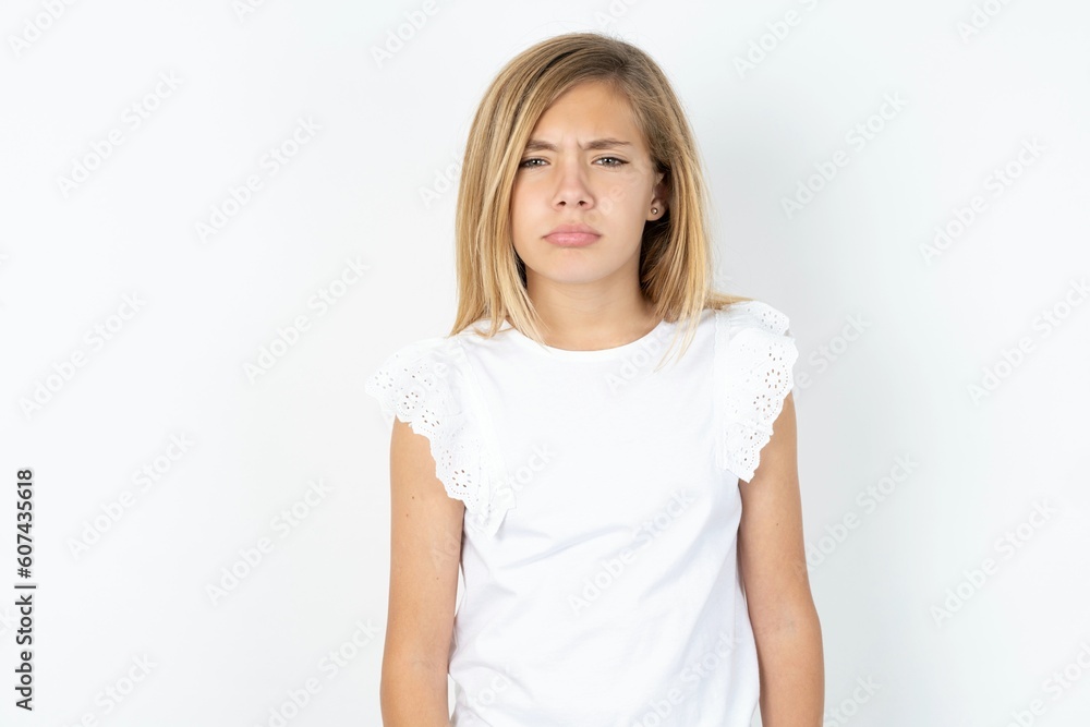 Offended dissatisfied beautiful caucasian teen girl wearing white T-shirt over white wall with moody displeased expression at camera being disappointed by something Offended dissatisfied beautiful caucasian teen girl wearing white T-shirt over white wall with moody displeased expression at camera being disappointed by something