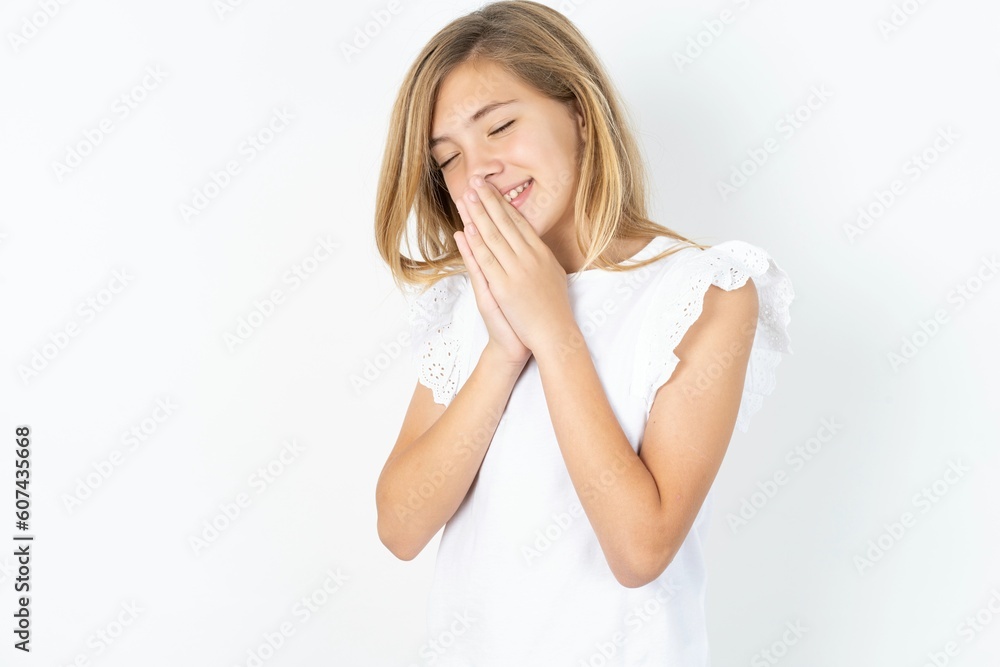 Overjoyed beautiful caucasian teen girl wearing white T-shirt over white wall laughs joyfully and keeps palms pressed together hears something funny Overjoyed beautiful caucasian teen girl wearing white T-shirt over white wall laughs joyfully and keeps palms pressed together hears something funny