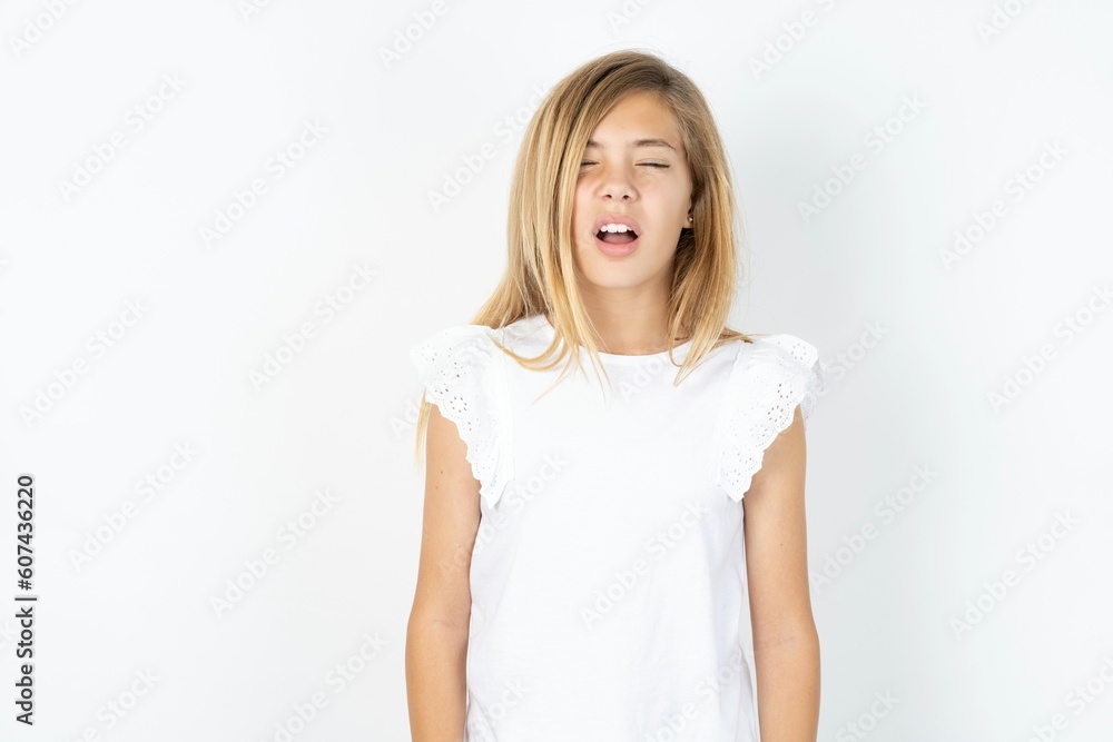 beautiful caucasian teen girl wearing white T-shirt over white wall yawns with opened mouth stands. Daily morning routine beautiful caucasian teen girl wearing white T-shirt over white wall yawns with opened mouth stands. Daily morning routine