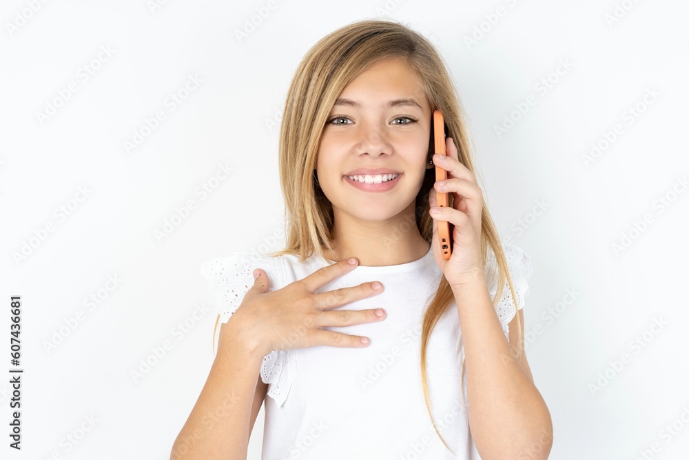 Smiling beautiful caucasian teen girl wearing white T-shirt over white wall talks via cellphone, enjoys pleasant great conversation. People, technology, communication concept Smiling beautiful caucasian teen girl wearing white T-shirt over white wall talks via cellphone, enjoys pleasant great conversation. People, technology, communication concept