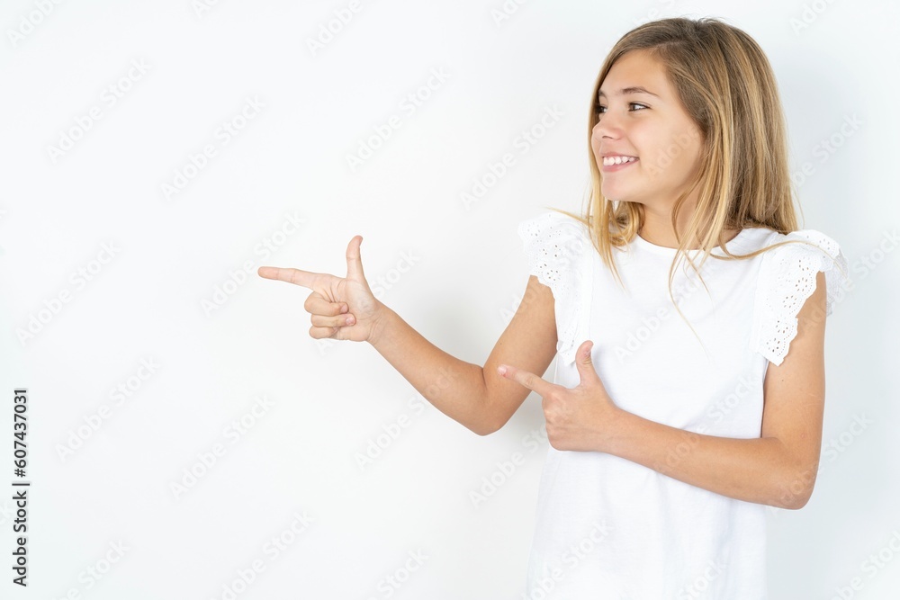 Optimistic beautiful caucasian teen girl wearing white T-shirt over white wall points with both hands and looking at empty space. Optimistic beautiful caucasian teen girl wearing white T-shirt over white wall points with both hands and looking at empty space.