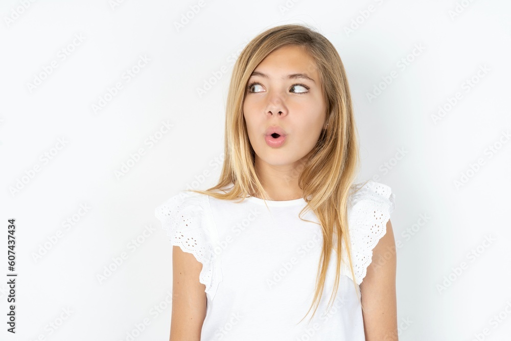 Shocked beautiful caucasian teen girl wearing white T-shirt over white wall look empty space with open mouth screaming: Oh My God! I can't believe this. Shocked beautiful caucasian teen girl wearing white T-shirt over white wall look empty space with open mouth screaming: Oh My God! I can't believe this.