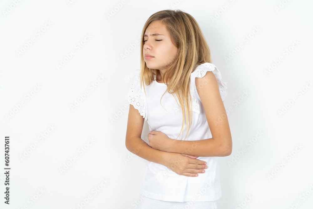 beautiful caucasian teen girl wearing white T-shirt over white wall got stomachache beautiful caucasian teen girl wearing white T-shirt over white wall got stomachache