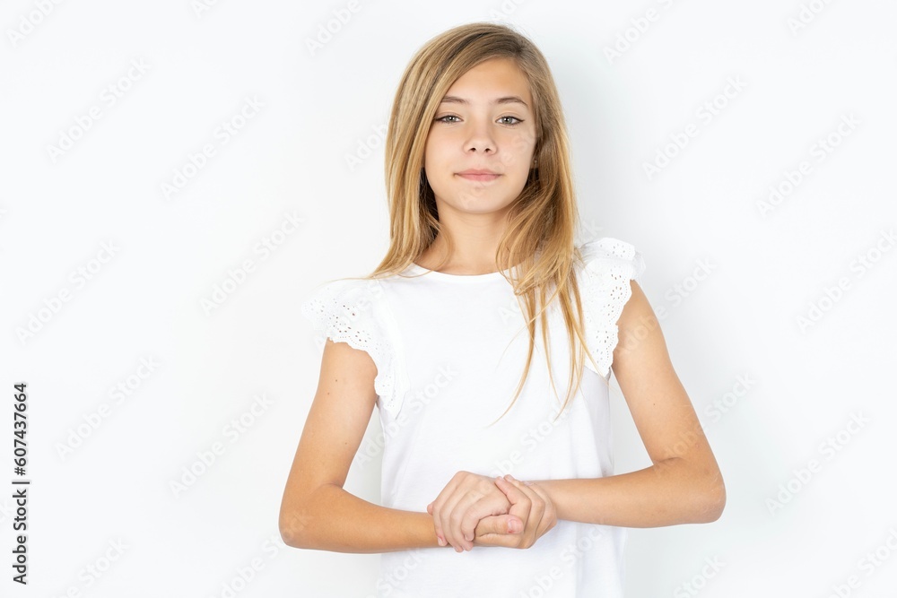 Photo of cheerful confident beautiful caucasian teen girl wearing white T-shirt over white wall arms together Photo of cheerful confident beautiful caucasian teen girl wearing white T-shirt over white wall arms together