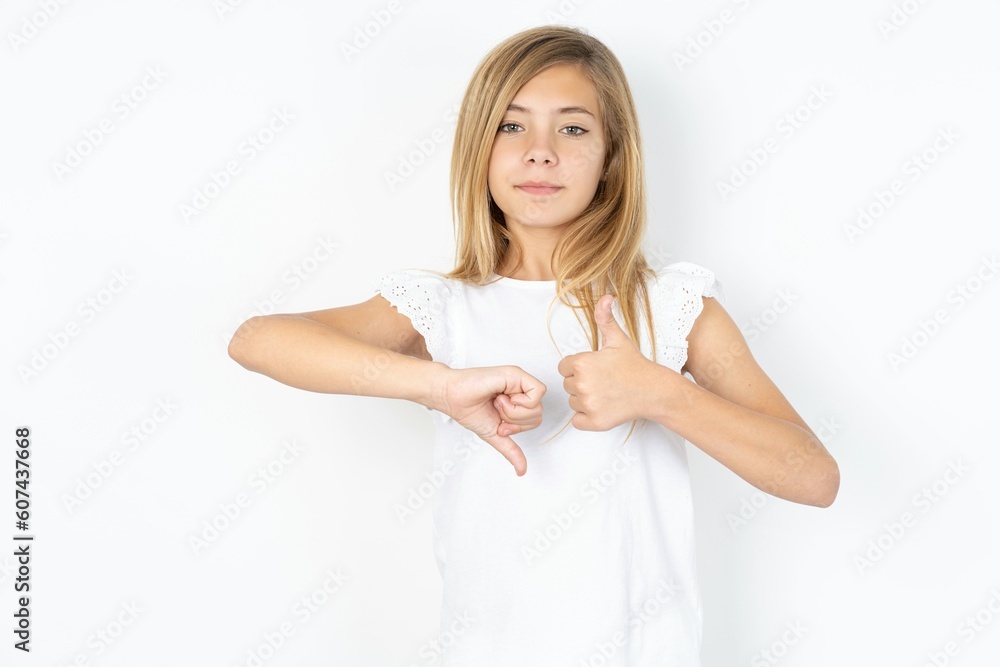beautiful caucasian teen girl wearing white T-shirt over white wall showing thumb up down sign beautiful caucasian teen girl wearing white T-shirt over white wall showing thumb up down sign