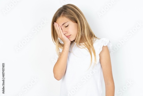 beautiful caucasian teen girl wearing white T-shirt over white wall with sad expression covering face with hands while crying. Depression concept.