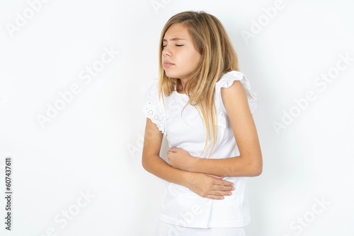 beautiful caucasian teen girl wearing white T-shirt over white wall got stomachache