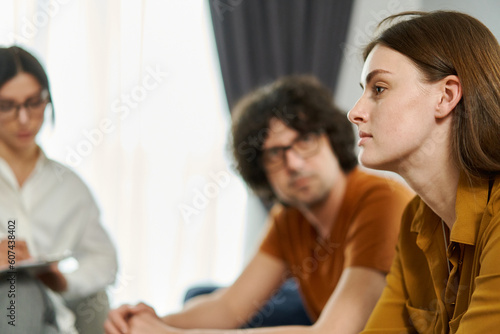 Close up portrait of frustrated pensive woman thinking over problems in relationships with boyfriend. Her partner and therapist on the background