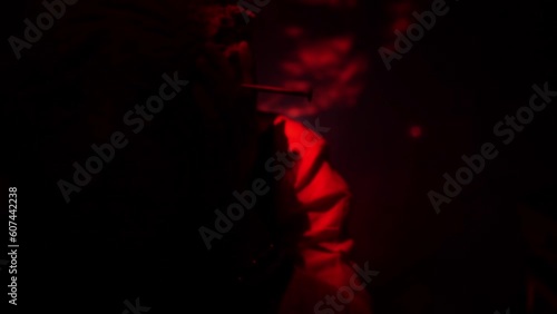 A man in a scary mask of an evil creature close-up. Red flickering light. Twilight. Demon mask on the face of a man with hands near his face. High quality FullHD footage