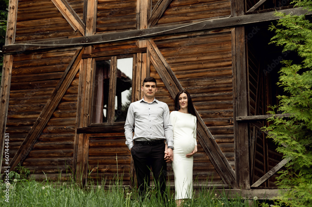 beautiful pregnant couple on the background of a wooden ecological house in the forest. a man hugs a pregnant woman. beautiful pregnant couple on the background of a wooden ecological house in the forest. a man hugs a pregnant woman.