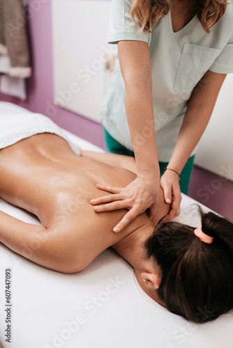 Beautiful young adult brunette receiving professional relaxation massage treatment at beauty spa salon.