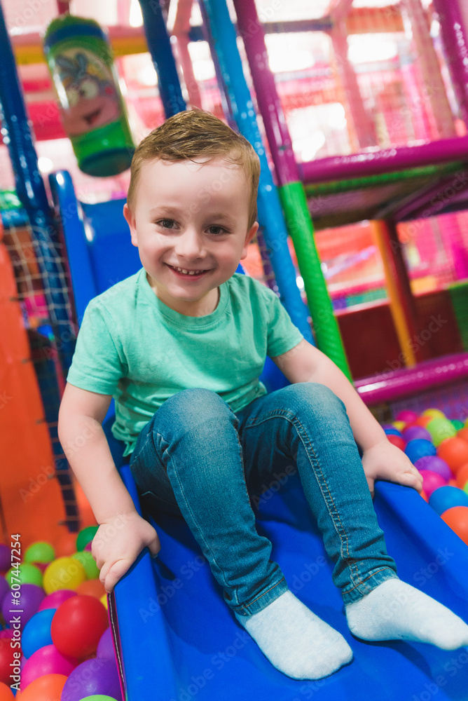Cheerful boy playing in slide and pool with colorful balls Cheerful boy playing in slide and pool with colorful balls