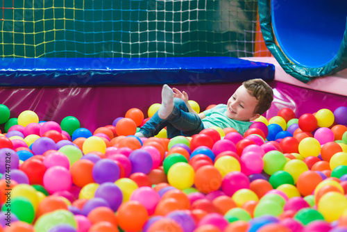 Happy laughing child laughing in an indoor play center. Children playing with colored balls in the playground ball pool. Party