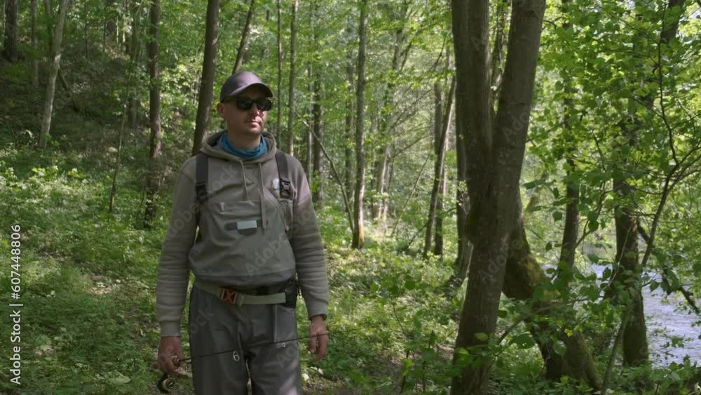 Fisherman walking along riverbank with spinning rod in his hands. Trout fishing. Fisherman walking along riverbank with spinning rod in his hands. Trout fishing.