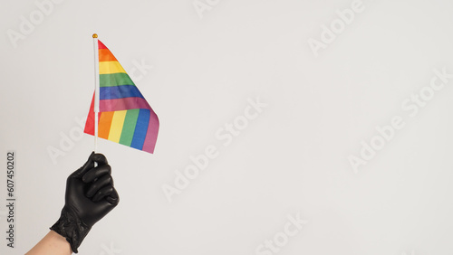 Hands are holding a rainbow flag. Hands are wearing black latex gloves