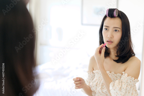 Beautiful young Asian woman applying makeup in front of the mirror. Lifestyle people concept. Advertisement for skin cream, anti-wrinkle cream, baby face