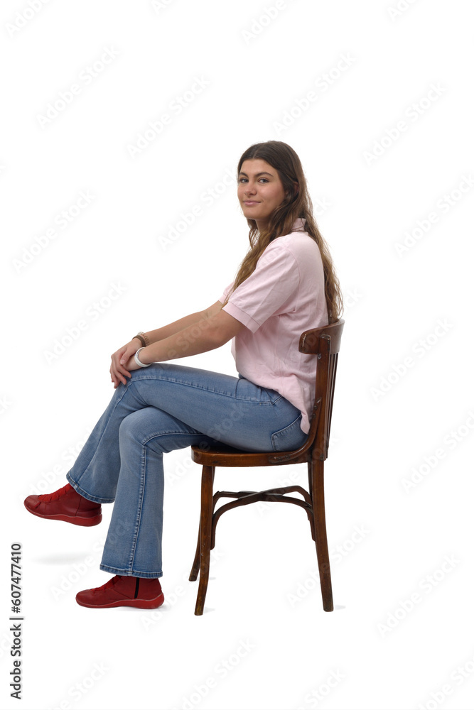 Side view of a young girl sitting on chair with cross legged and looking at camera on white background Side view of a young girl sitting on chair with cross legged and looking at camera on white background
