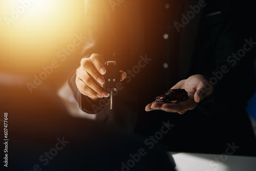 A car rental company employee is handing out the car keys to the renter after discussing the rental details and conditions together with the renter signing a car rental agreement. Concept car rental.