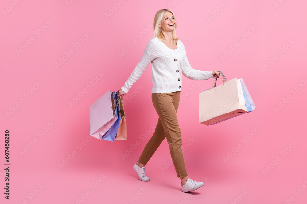 Fototapeta premium Full body profile portrait of positive pretty lady hold bags walking isolated on pink color background